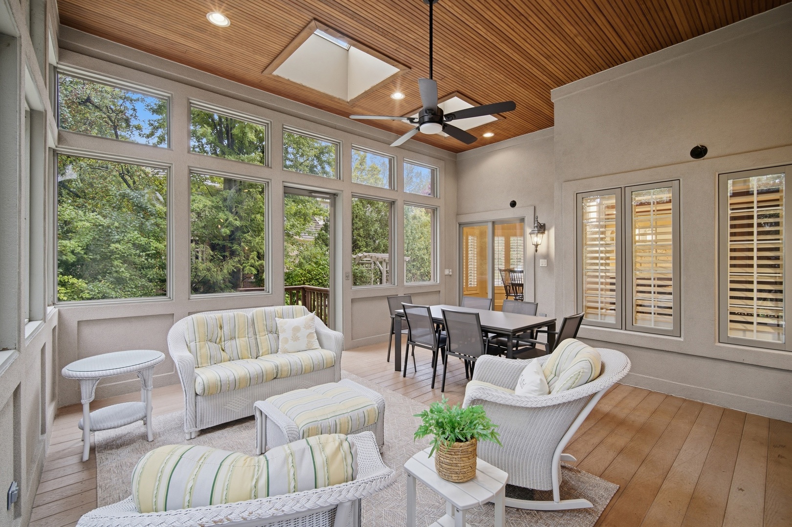 Sunroom with wicker seating, tall windows overlooking trees, and a wood-plank ceiling.
