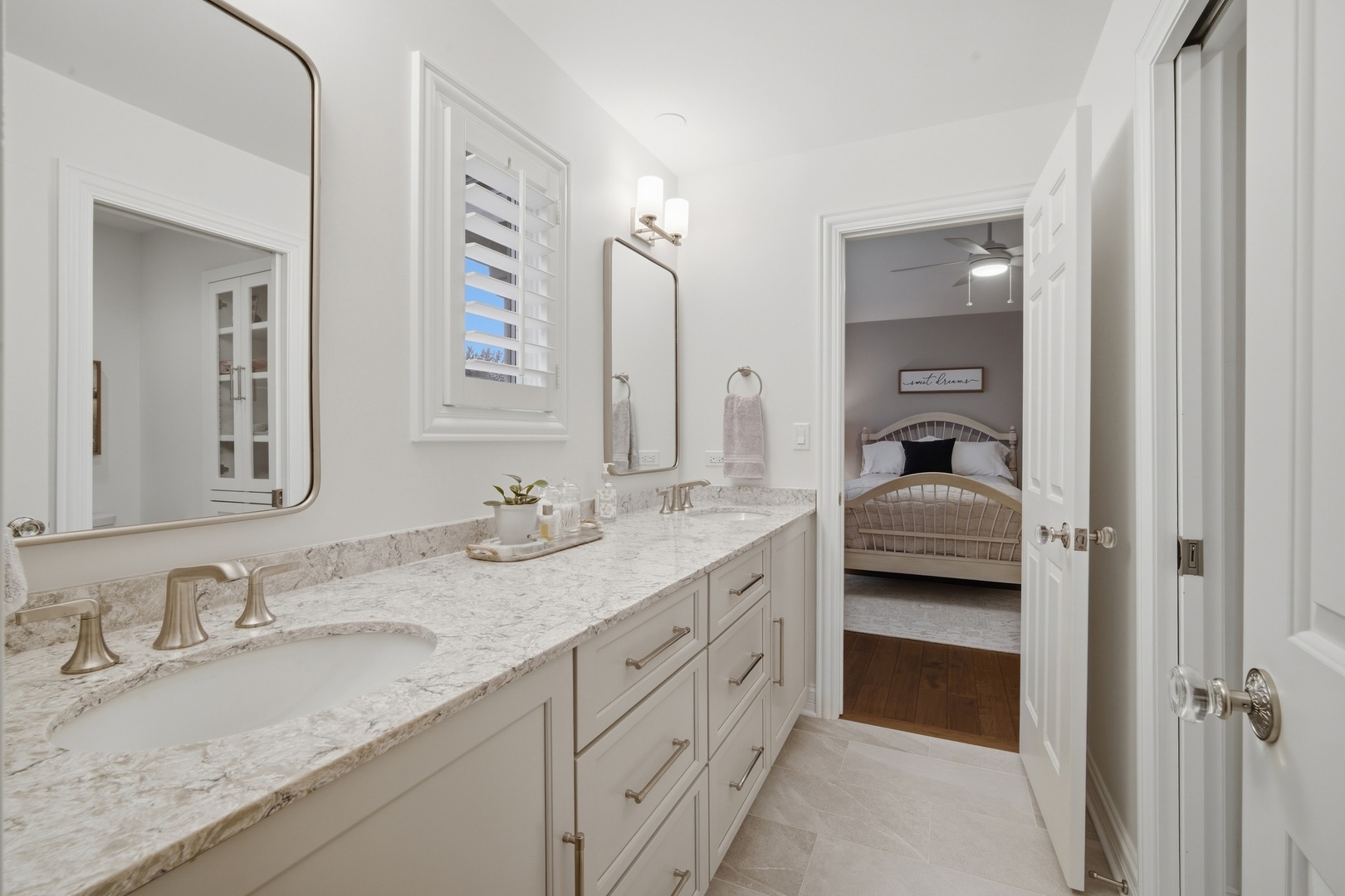 Bathroom with a long marble-look double vanity and a view into a bedroom.