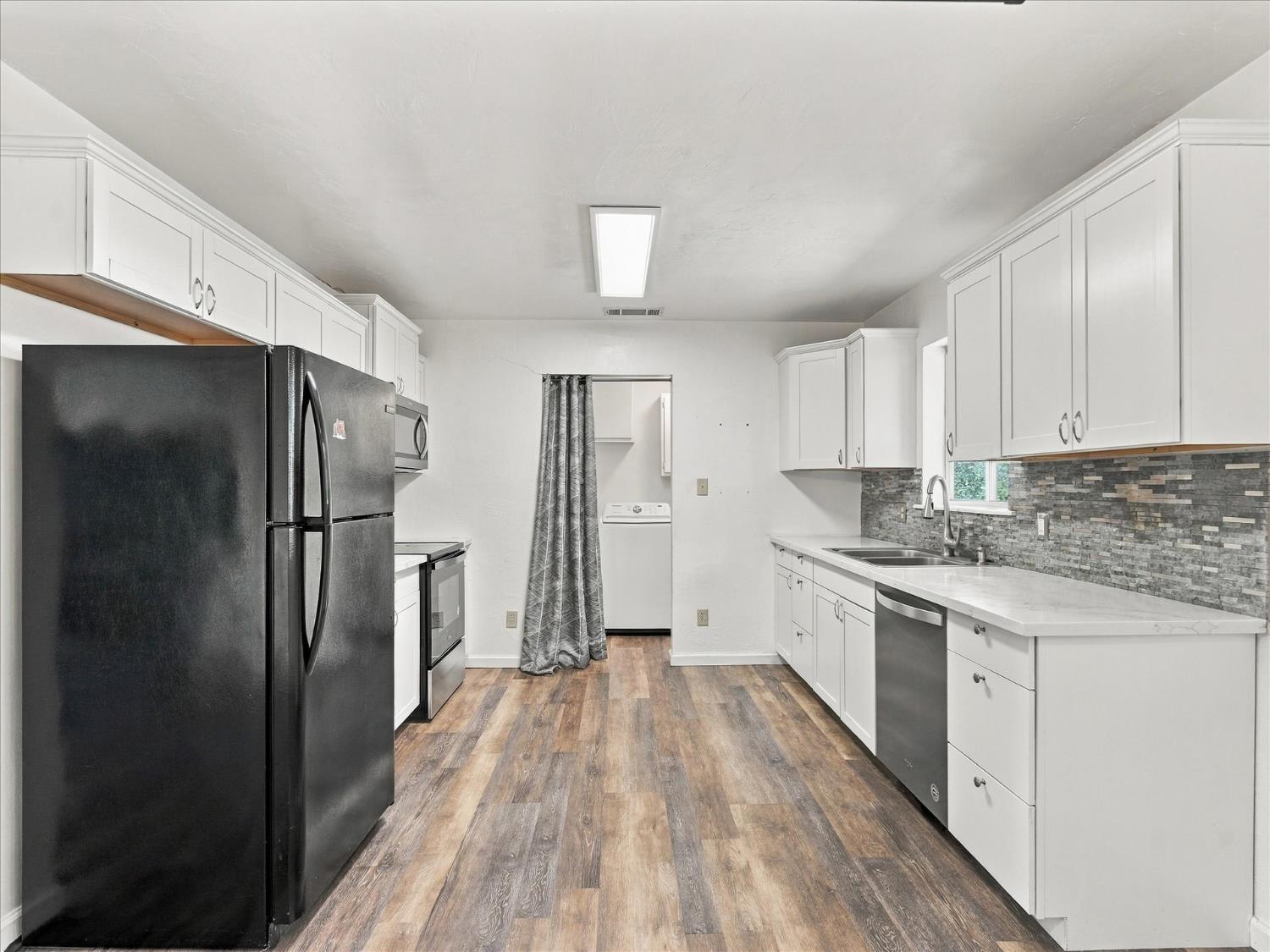 Kitchen with white cabinets, dark appliances, gray tile backsplash, and wood-look flooring.
