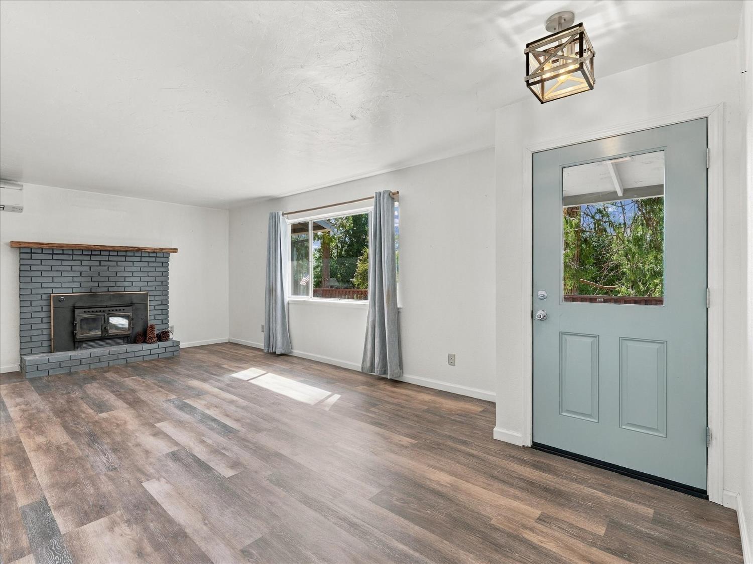 Empty living room with gray brick fireplace, wood stove, and blue-gray front door.