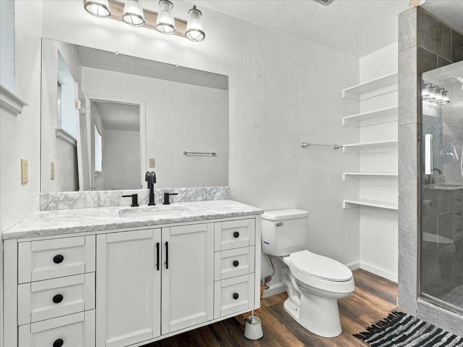 Bathroom with a white vanity and marble-pattern counter beside a glass-enclosed gray tile shower.
