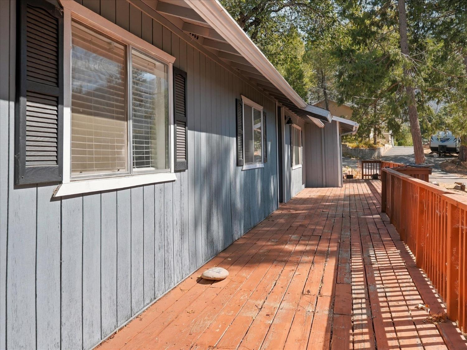 Home exterior with a long reddish wood deck, matching railings, and gray siding.