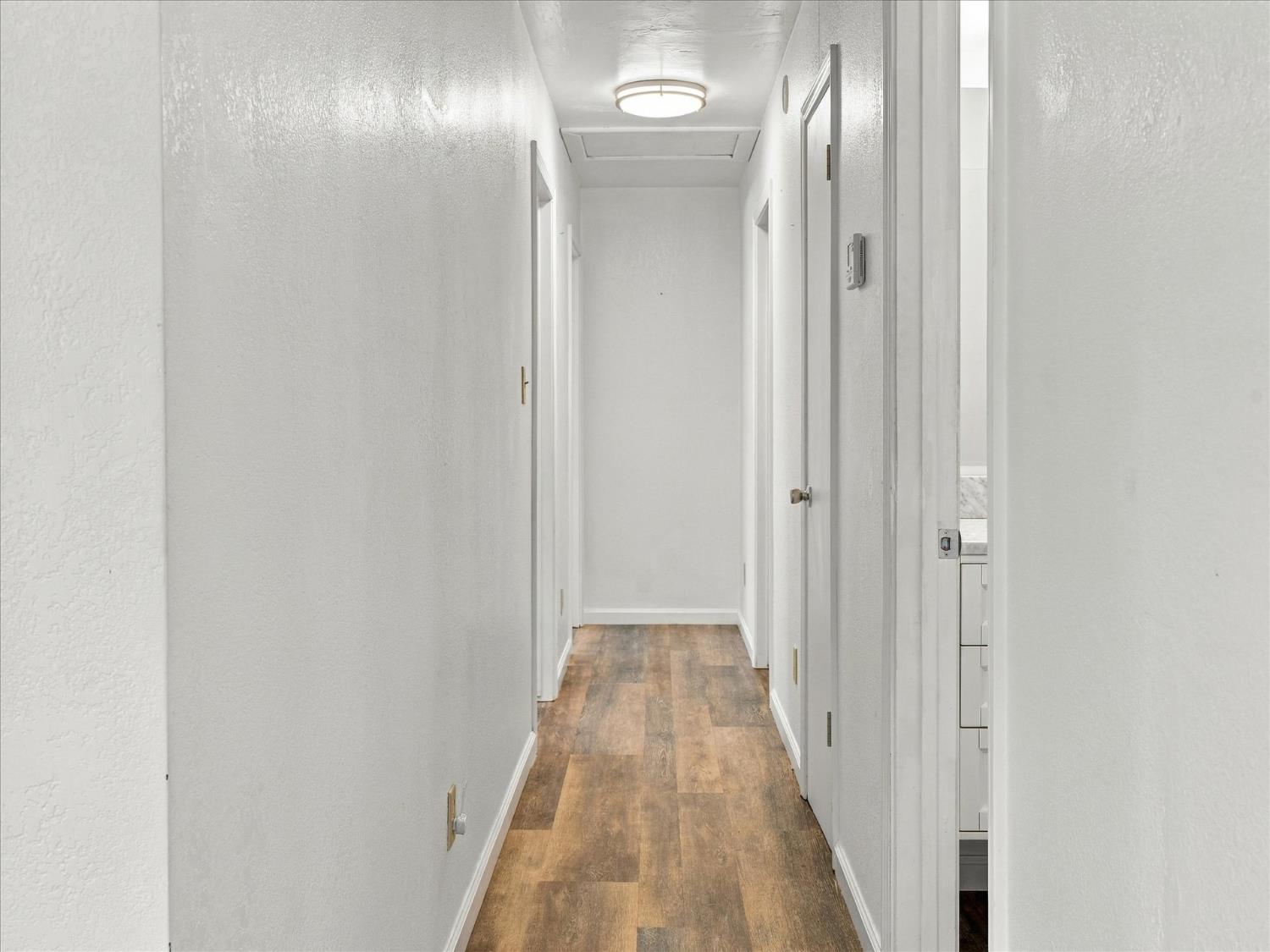 Hallway with brown wood-look flooring, white walls, and multiple doorways.