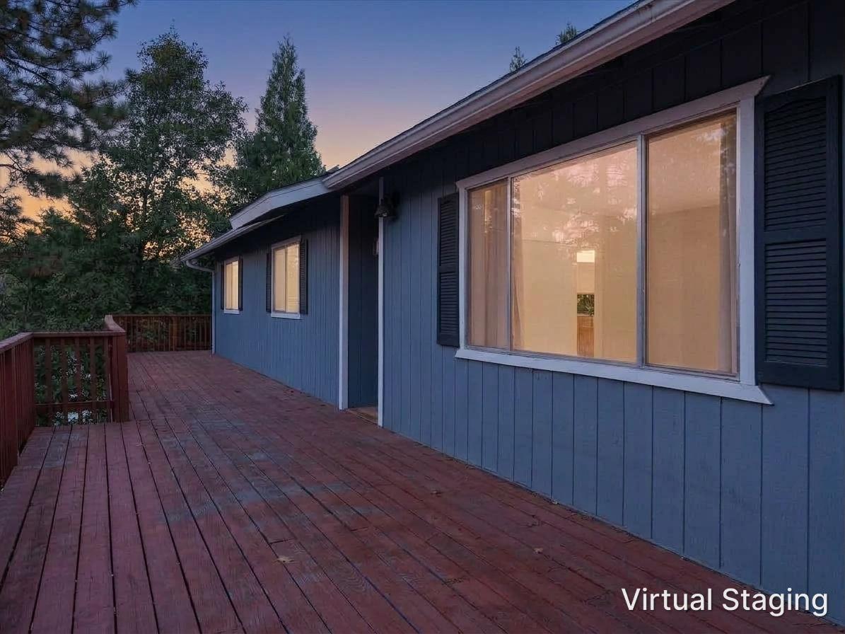 Blue-sided house and empty redwood deck among trees at dusk.