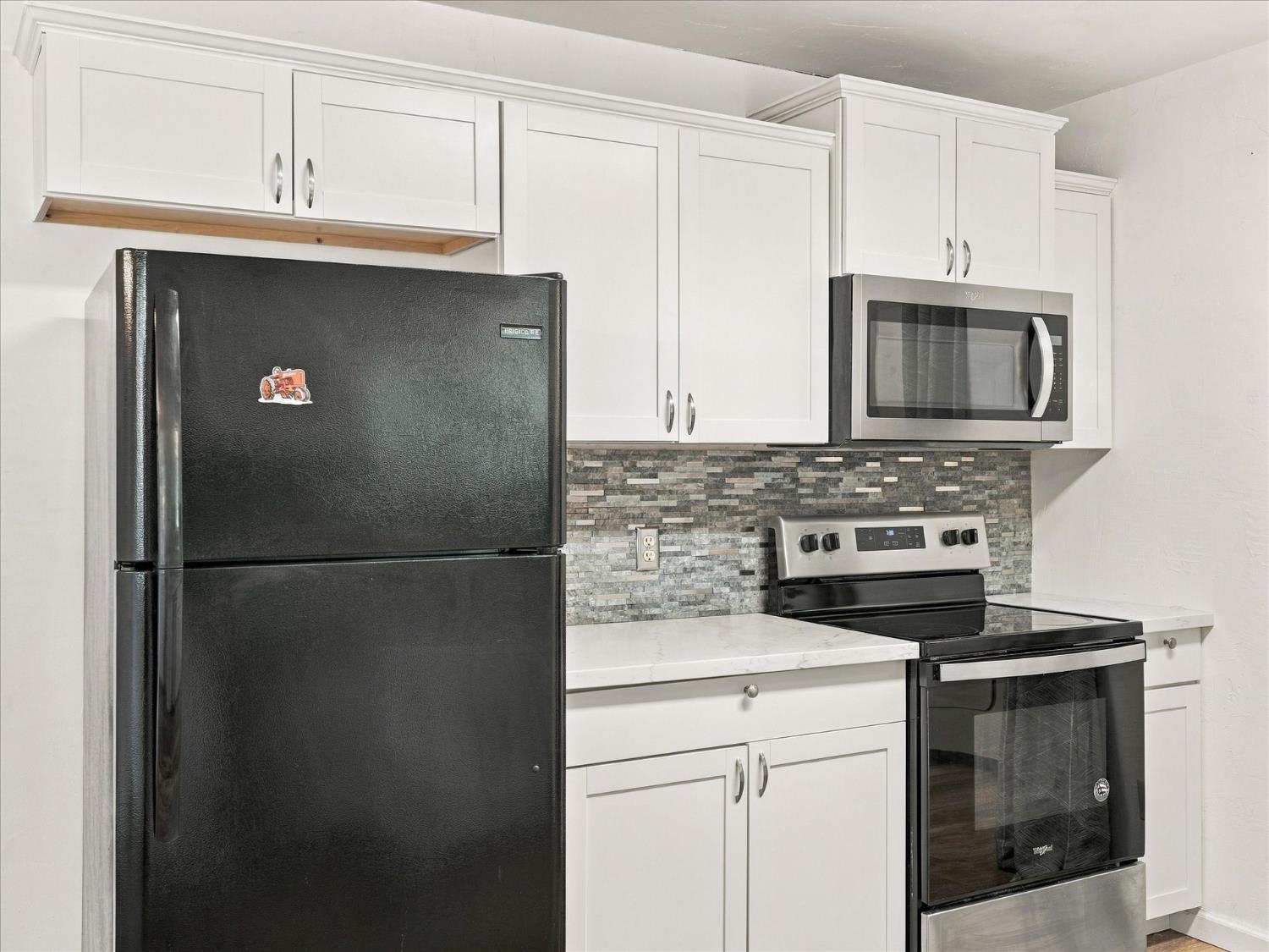 Kitchen with white cabinets, a gray mosaic backsplash, and black appliances.