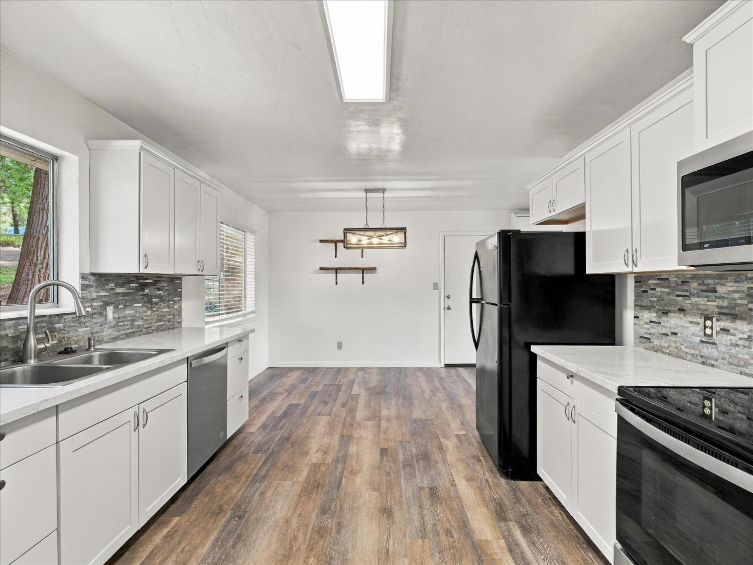 Kitchen with white cabinets, gray mosaic backsplash, wood-look floors, and black appliances.