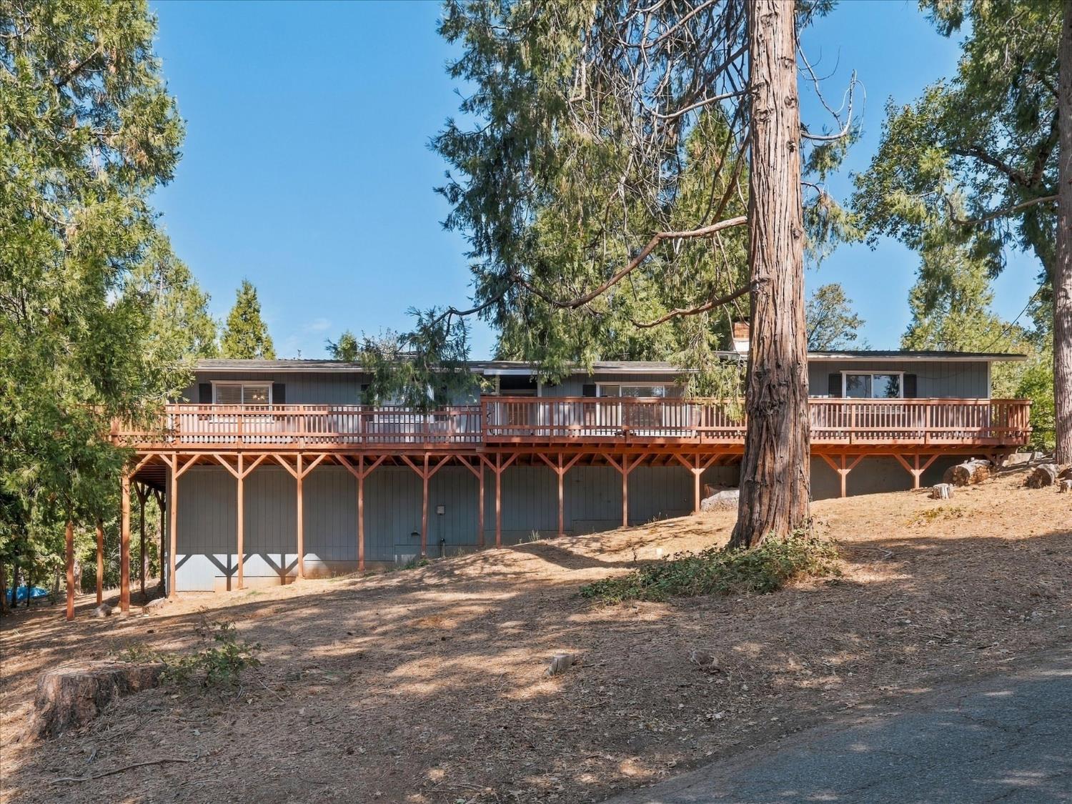 Home with a long raised wooden deck on a sloping, tree-covered lot.
