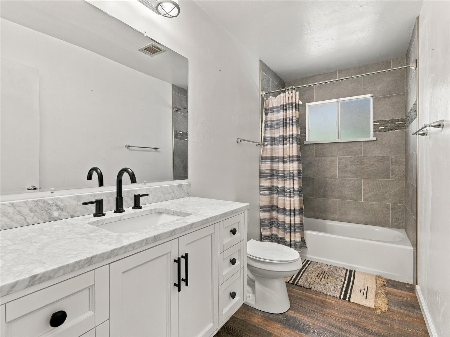 Bathroom with a white vanity and marble-look counter beside a gray-tiled tub-shower.
