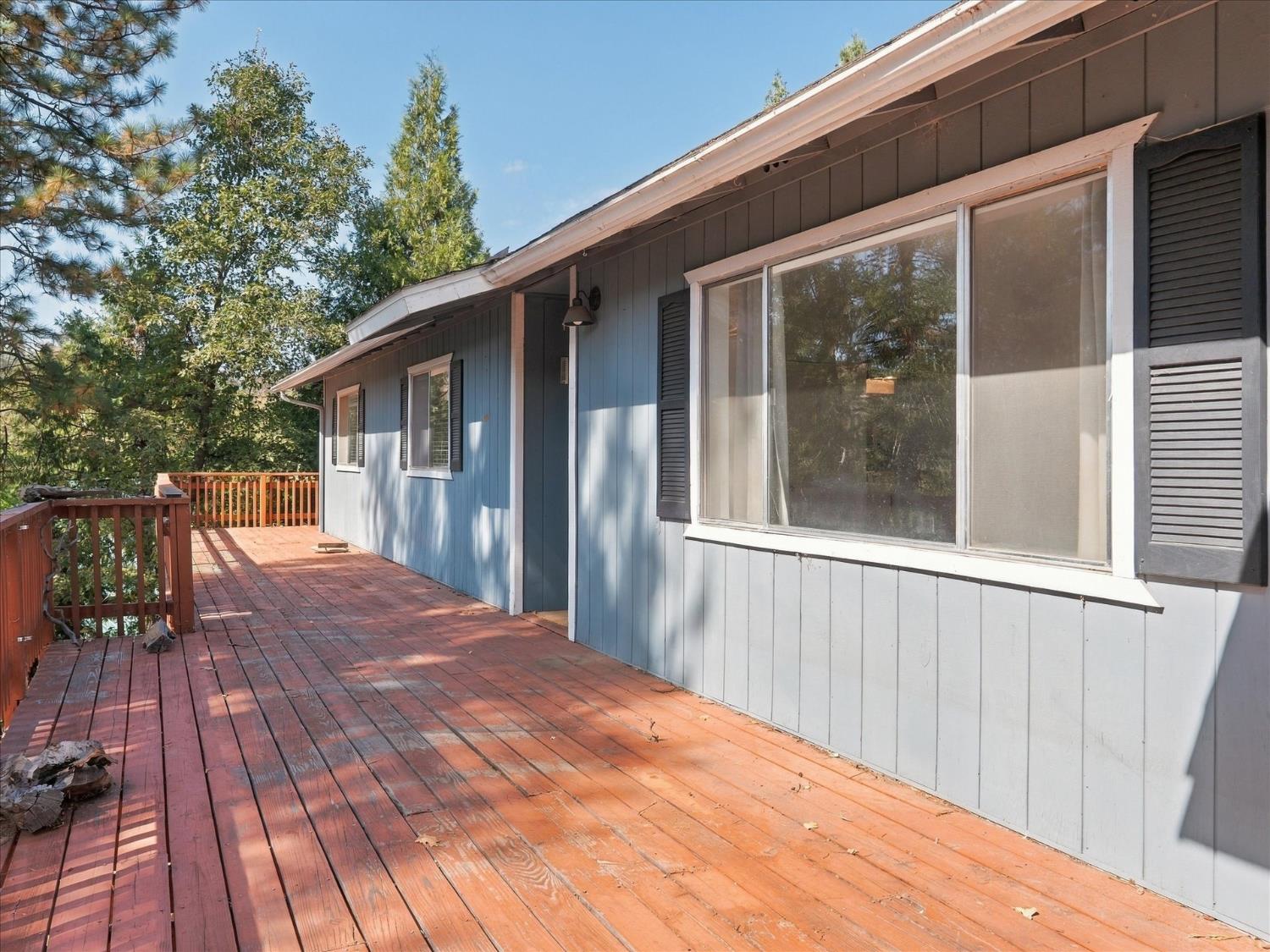 Wooden deck beside a blue-sided house with large windows and surrounding trees.