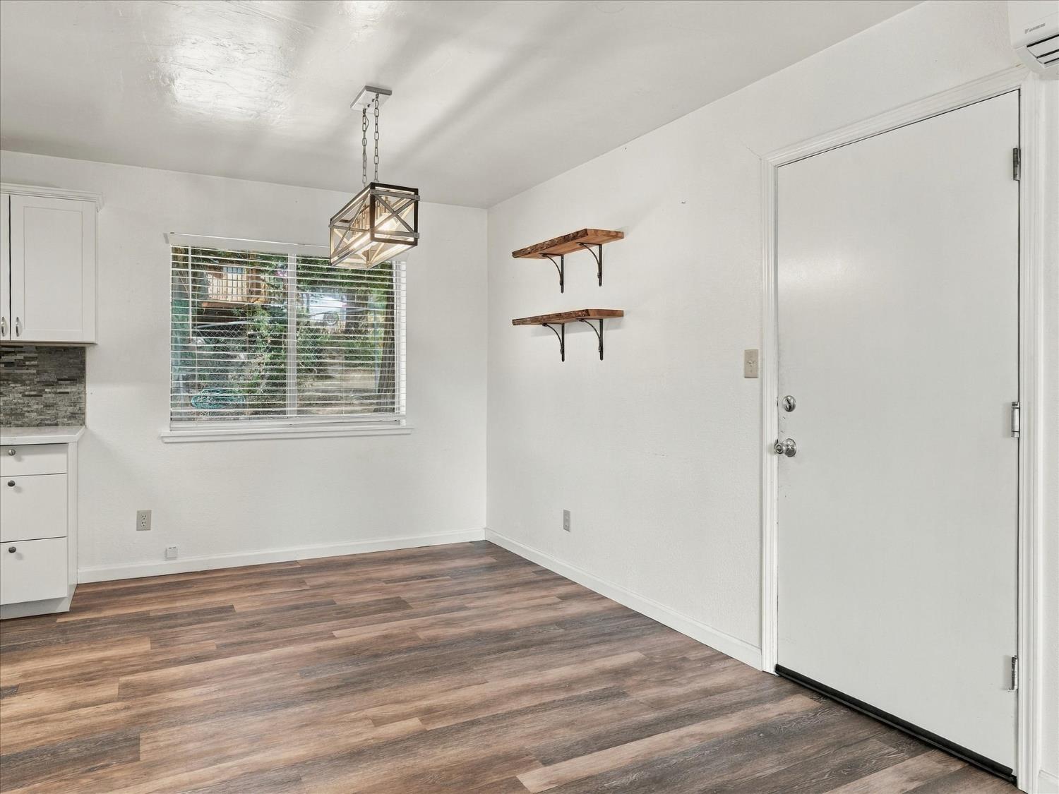 Empty dining area with wood-look flooring, a window with blinds, and a geometric pendant light.