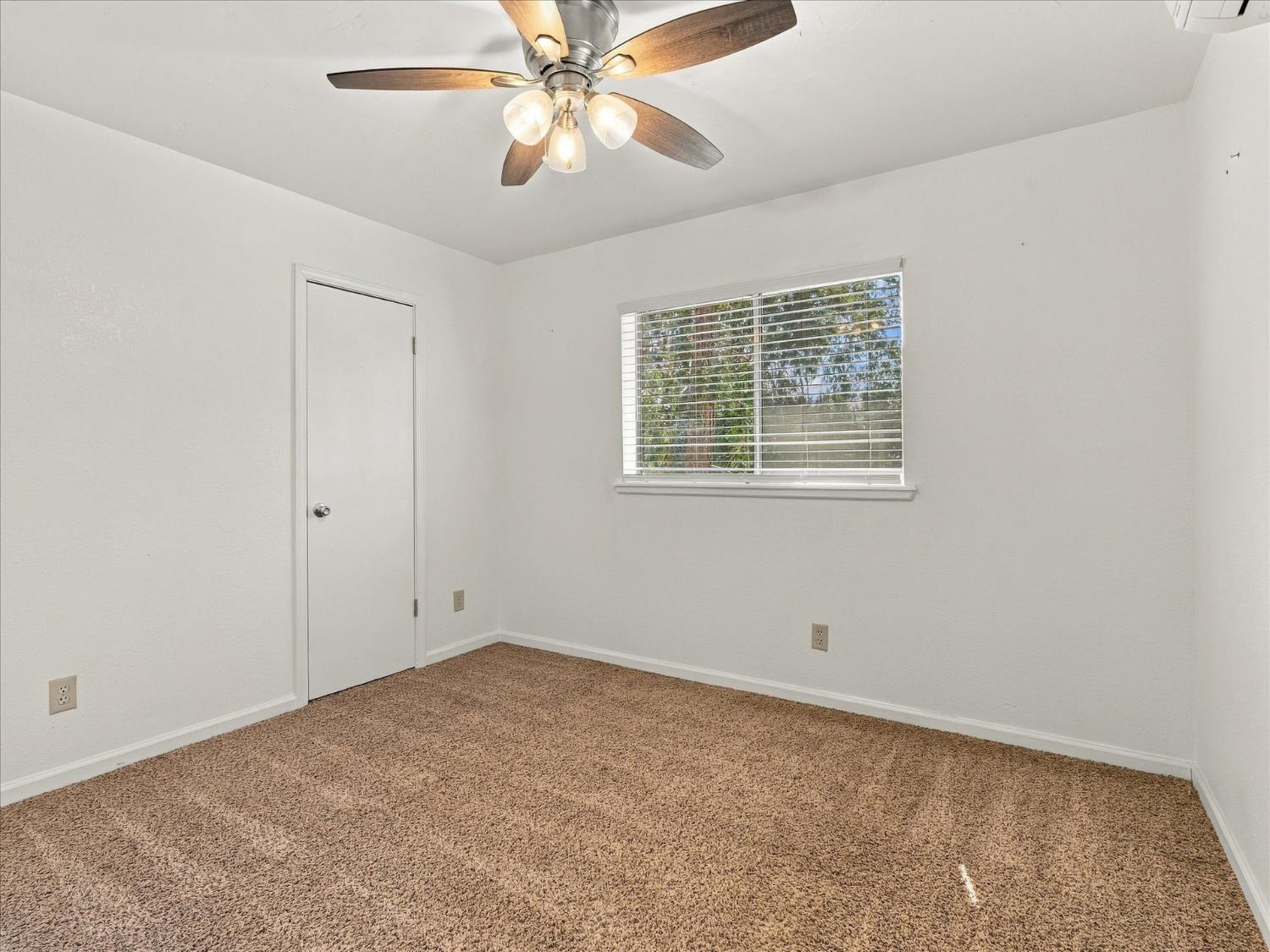 Empty bedroom with beige carpet, window blinds, and a ceiling fan with lights.