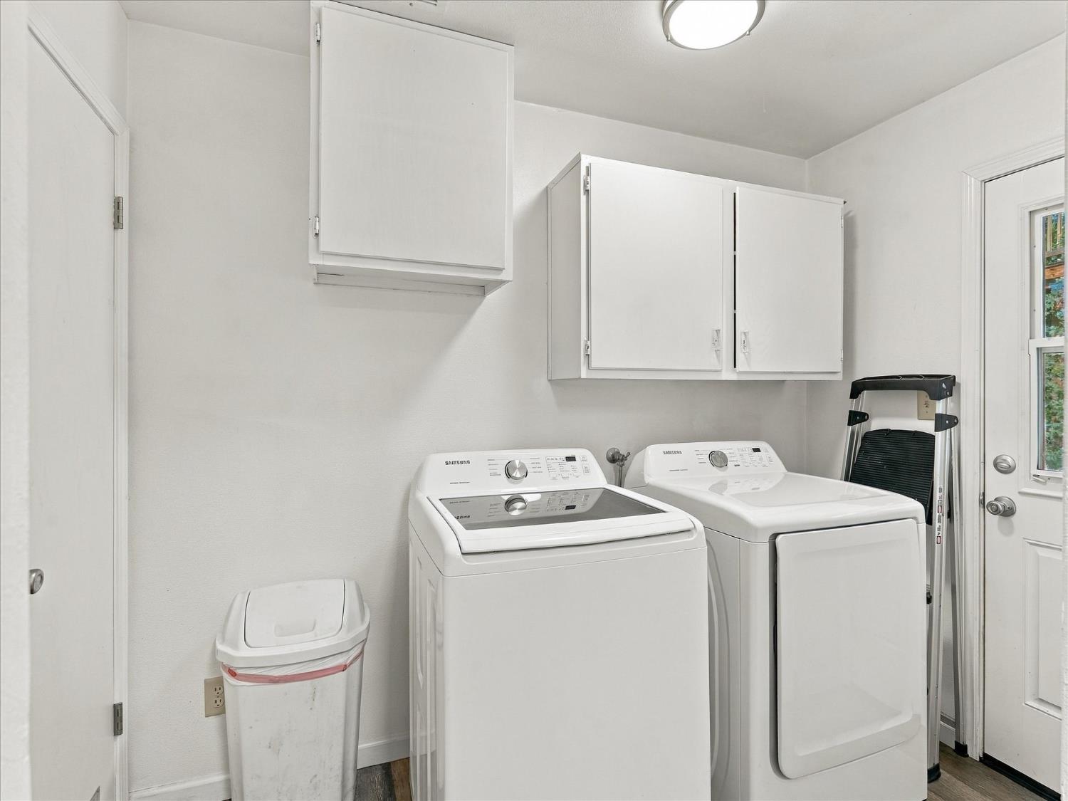 Laundry room with matching white Samsung washer and dryer beneath wall cabinets.