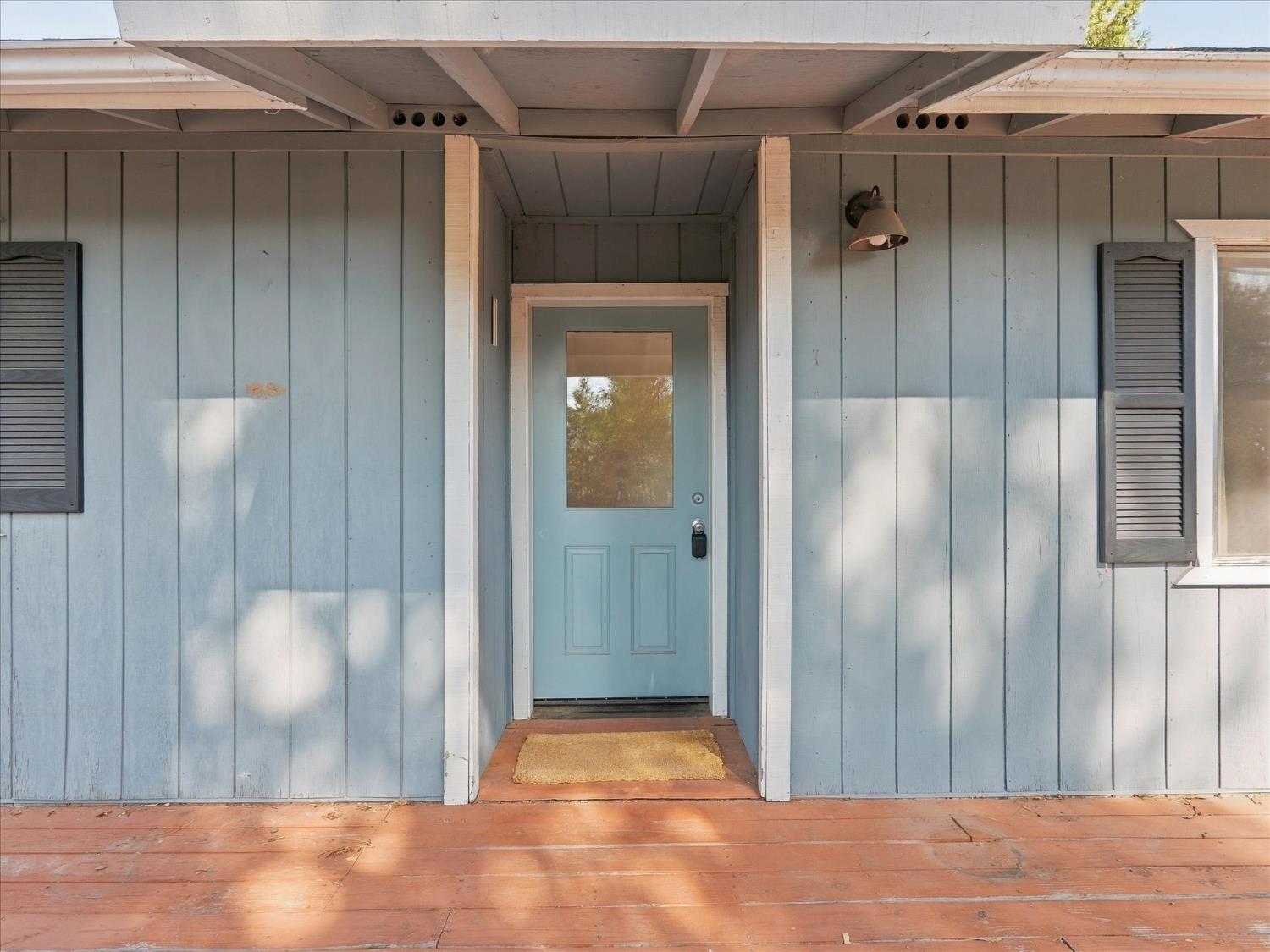 Light blue house entrance with a recessed blue door, white trim, and covered wooden porch.