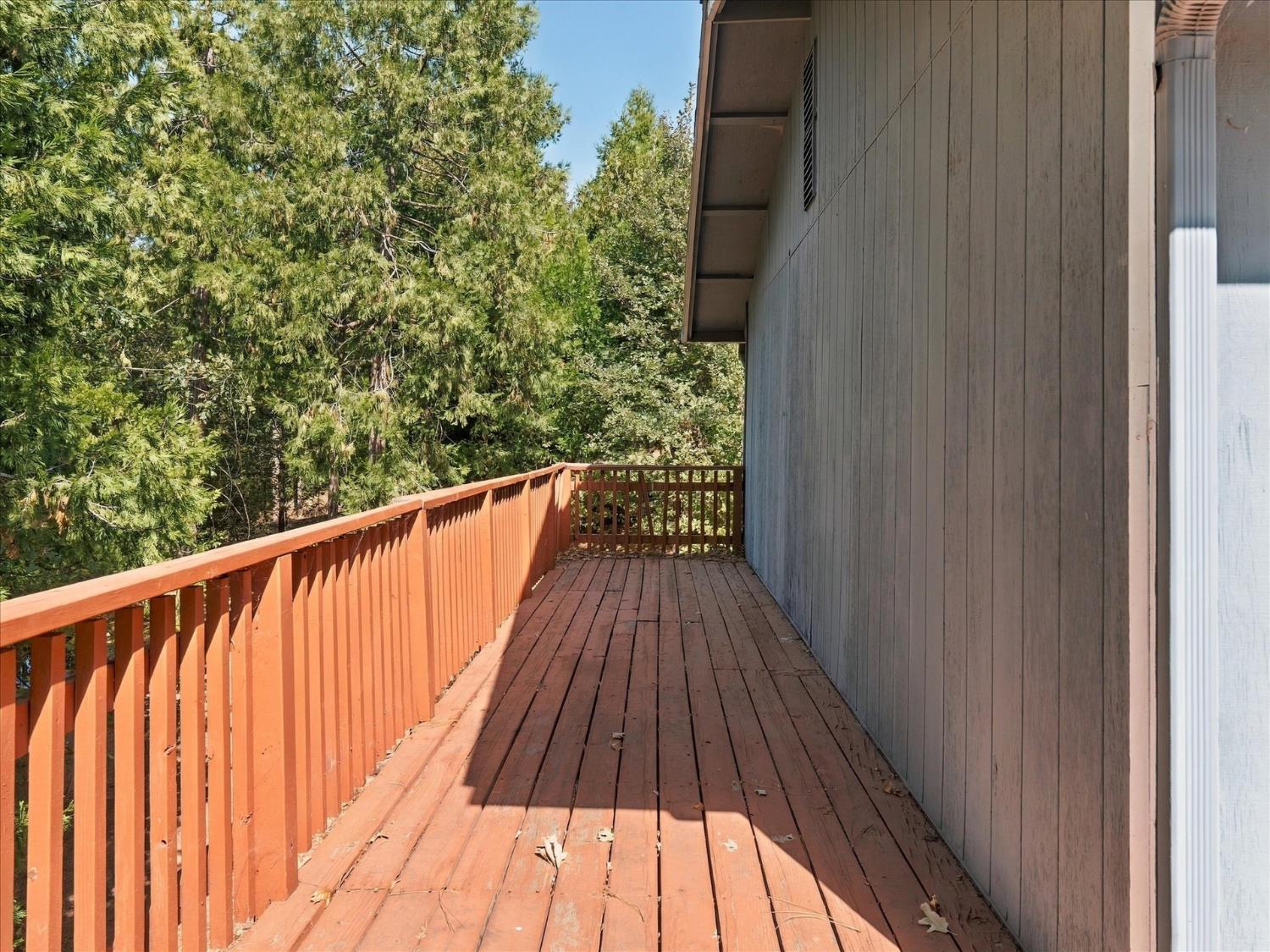 Weathered wooden deck beside the home, bordered by a railing and dense trees.