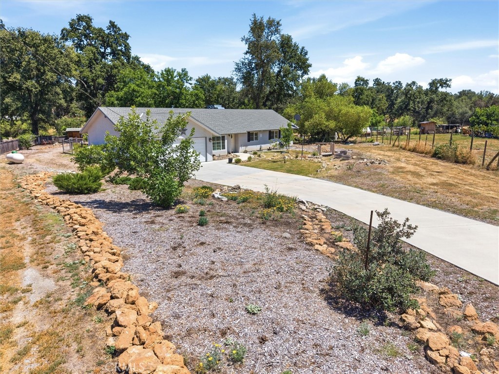Single-story home with a concrete driveway, rock-edged landscaping, and a spacious rural yard.