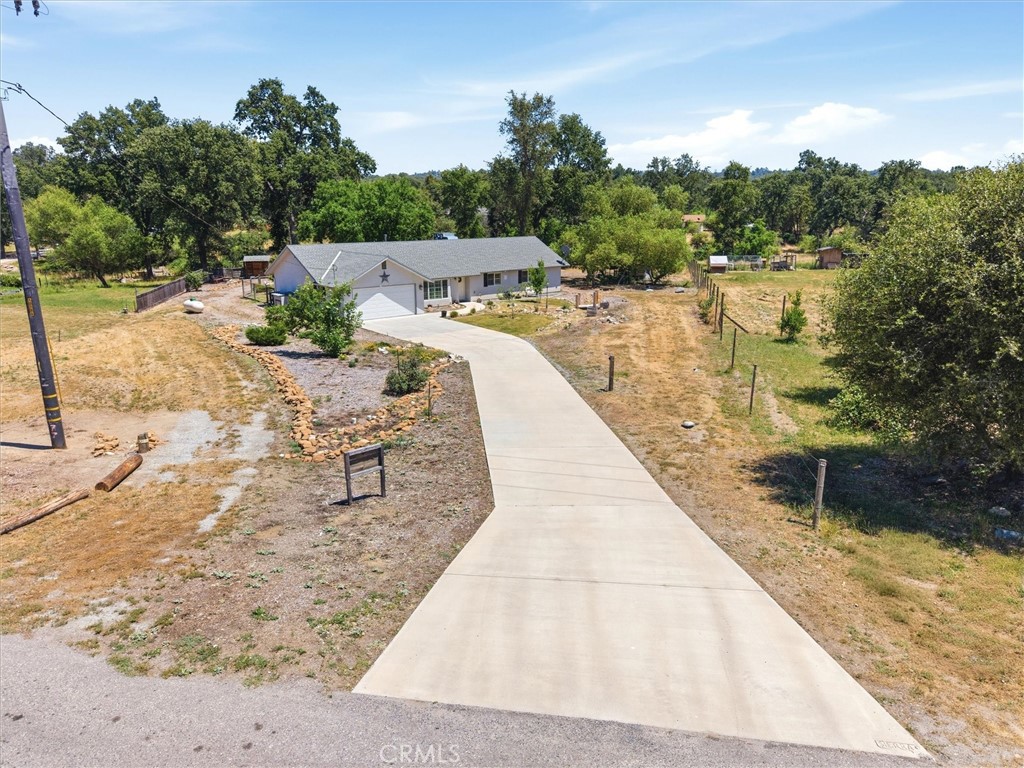 Aerial view of a single-story home with a long curved driveway and dry, tree-lined grounds.