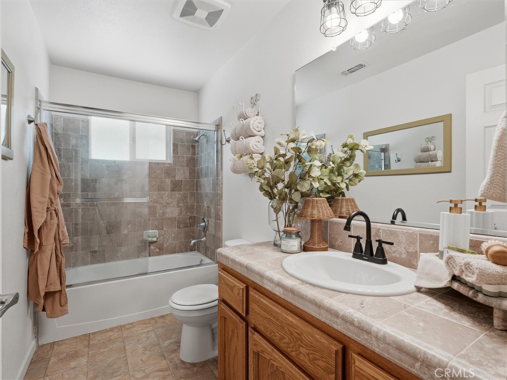 Bathroom with a tiled tub and shower, glass enclosure, and wood vanity with a white sink.