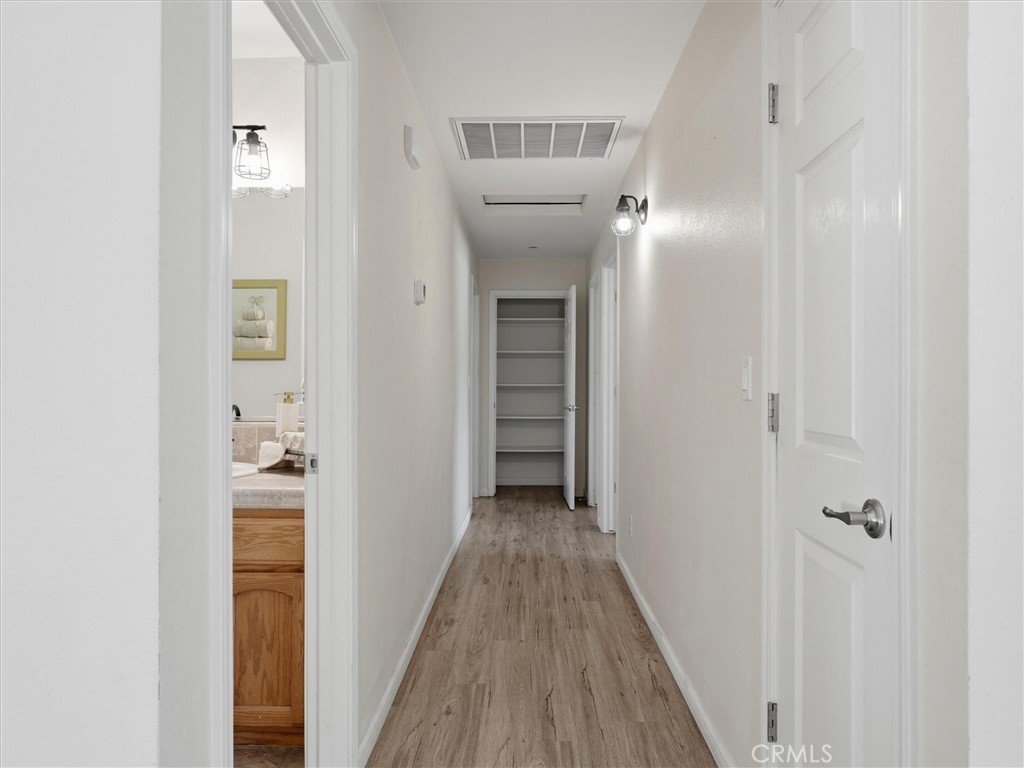 Hallway with light wood-look flooring, built-in shelves, and a glimpse of a bathroom vanity.