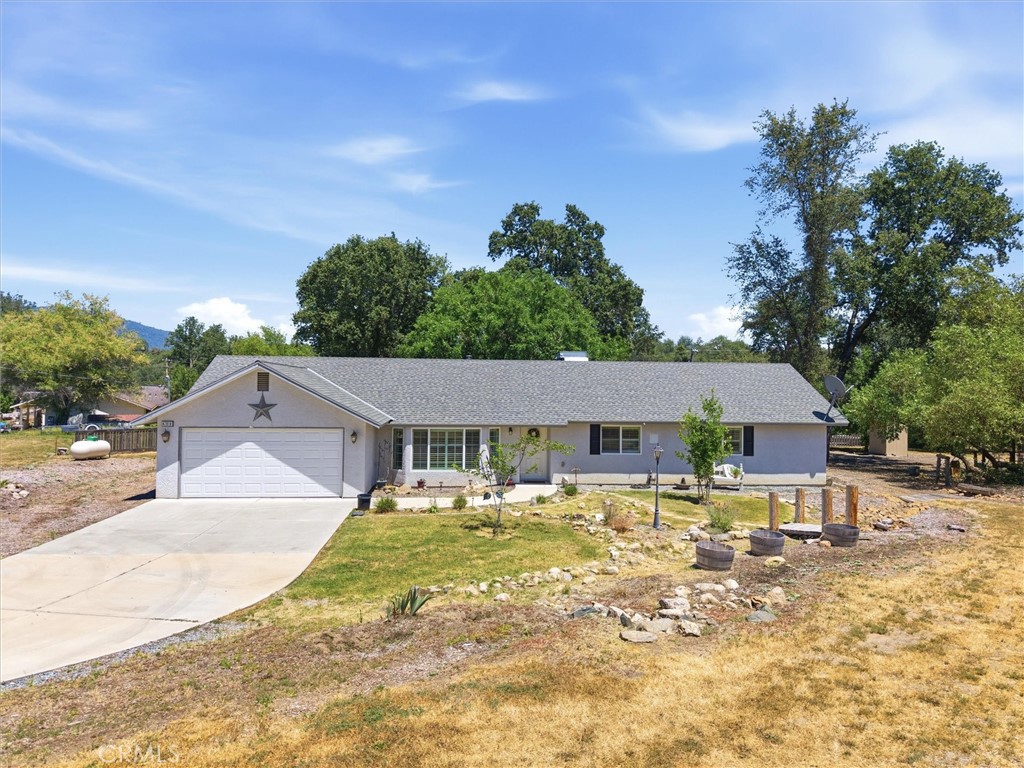 Single-story gray house with an attached garage, broad driveway, and mature trees.