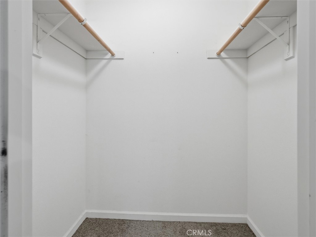 Empty walk-in closet with wooden hanging rods and shelves along both sides.