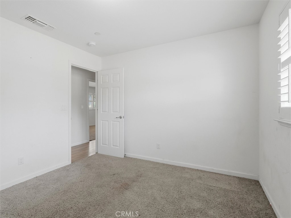 Empty bedroom with beige carpet, white walls, and a window with white shutters.