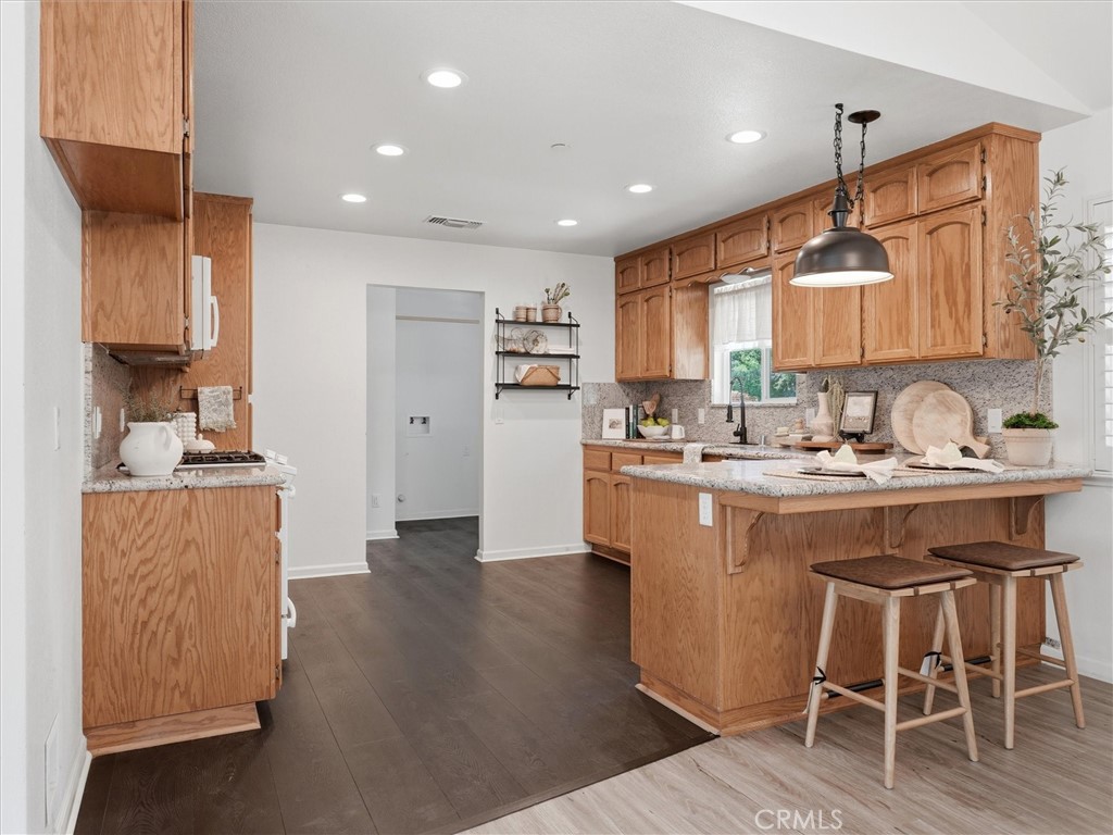 Kitchen with honey-toned wood cabinets, granite counters, and a central island with bar stools.