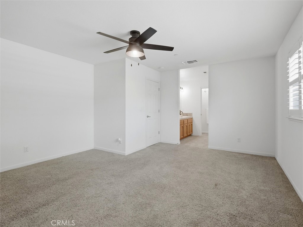 Empty carpeted bedroom with a dark ceiling fan and bathroom vanity visible through the doorway.