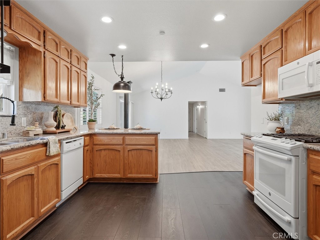 Kitchen with warm wood cabinets, granite countertops, white appliances, and an open living area.