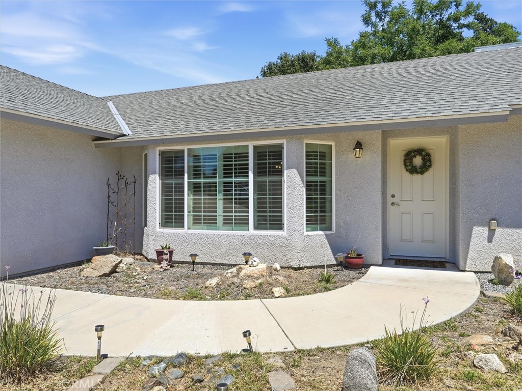Home entrance with a wreath-adorned white door, shuttered windows, and a curved concrete walkway.