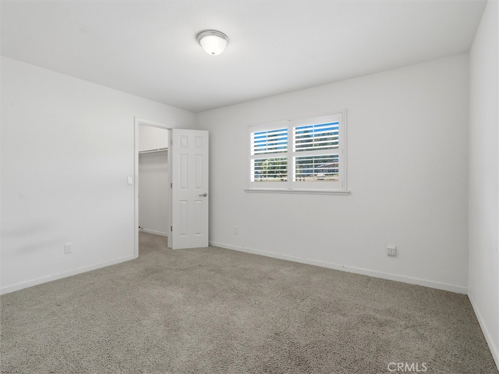 Empty bedroom with beige carpet, plantation shutters, and an open closet door.