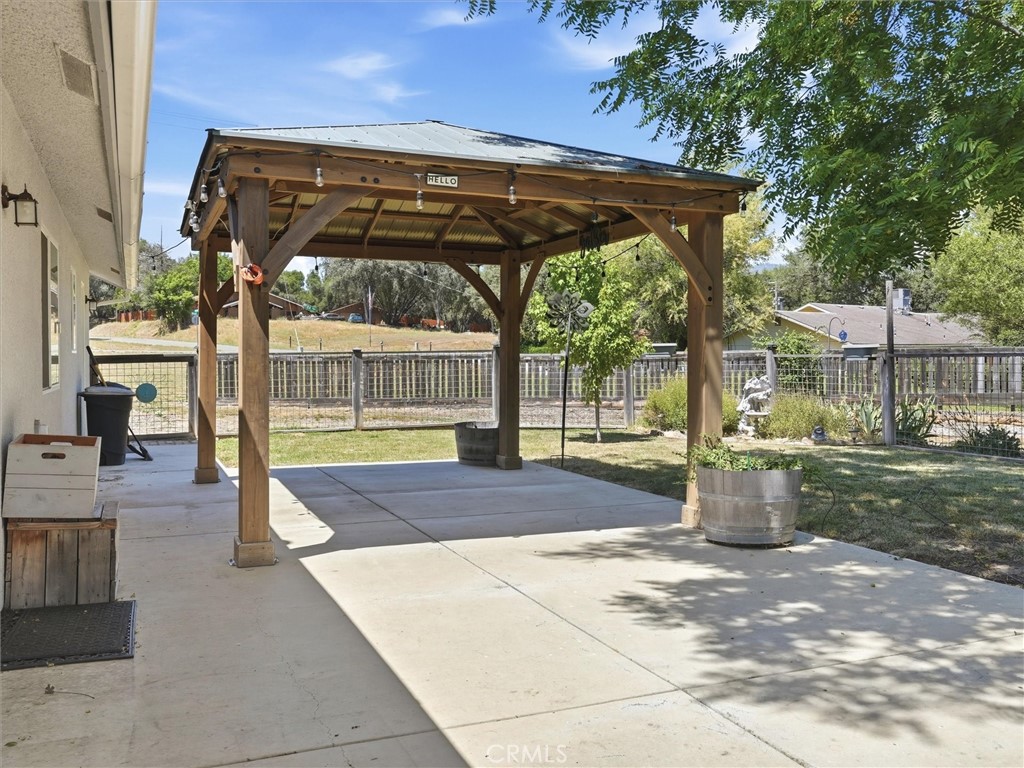 Concrete backyard patio beneath a wooden pergola, with a fenced yard and barrel planter.