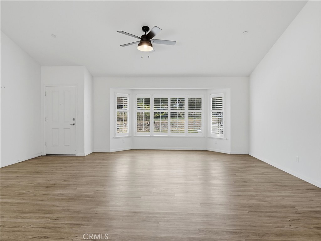 Empty living room with wide shuttered windows, light wood-look flooring, and a ceiling fan.