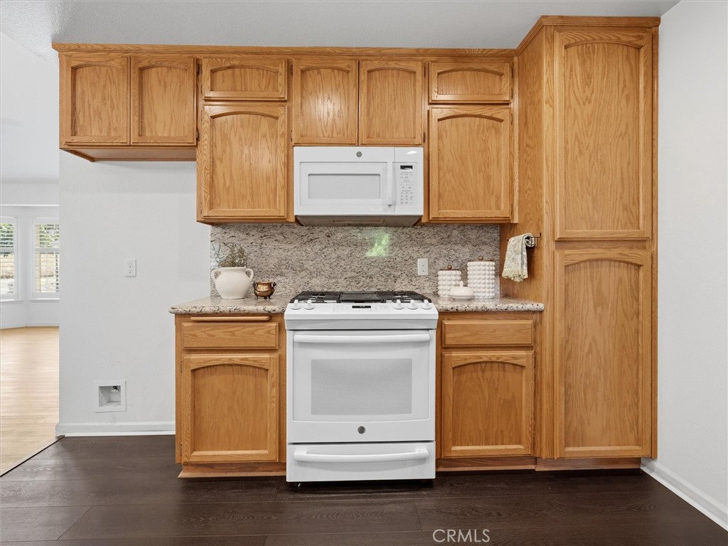 Kitchen with honey-colored cabinets, speckled stone backsplash, and white appliances.