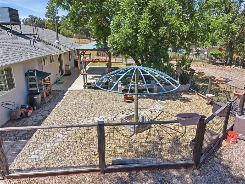 Fenced gravel backyard with a circular blue metal frame, curved stone path, and covered patio.