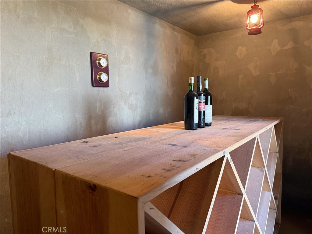 Rustic wine cellar with a long wooden counter, open shelving, and three wine bottles.