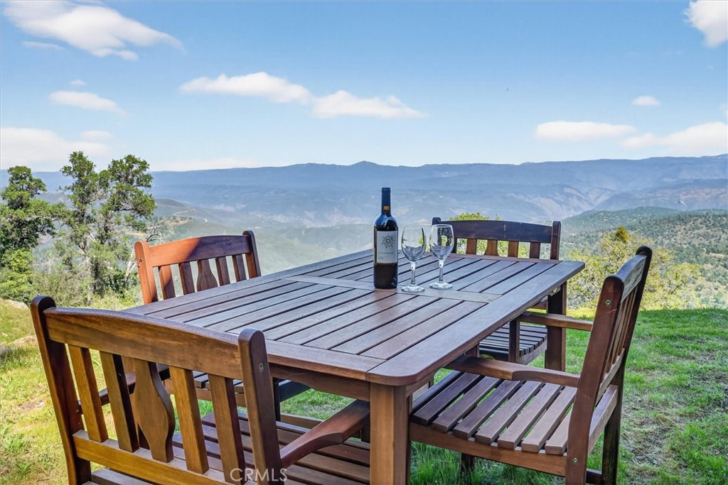 Outdoor dining table set with wine overlooks green foothills and distant mountains.