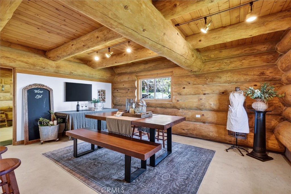 Log cabin dining room with exposed timber beams, a wooden table, and a chalkboard wine list.