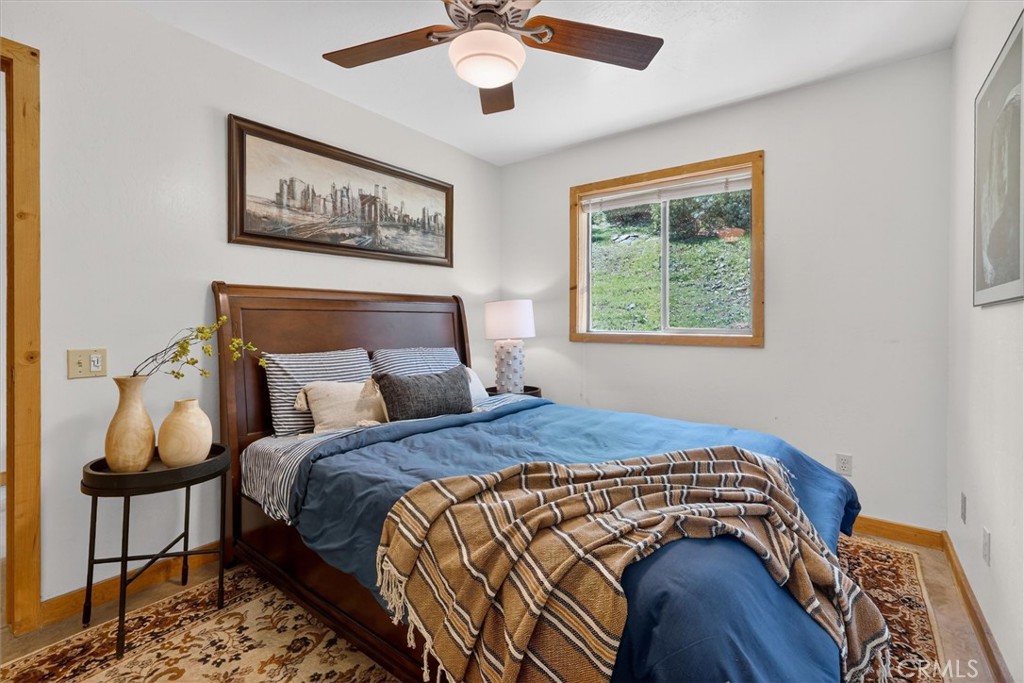 Furnished bedroom with blue bedding, a dark wood bed, and a window overlooking a green hillside.