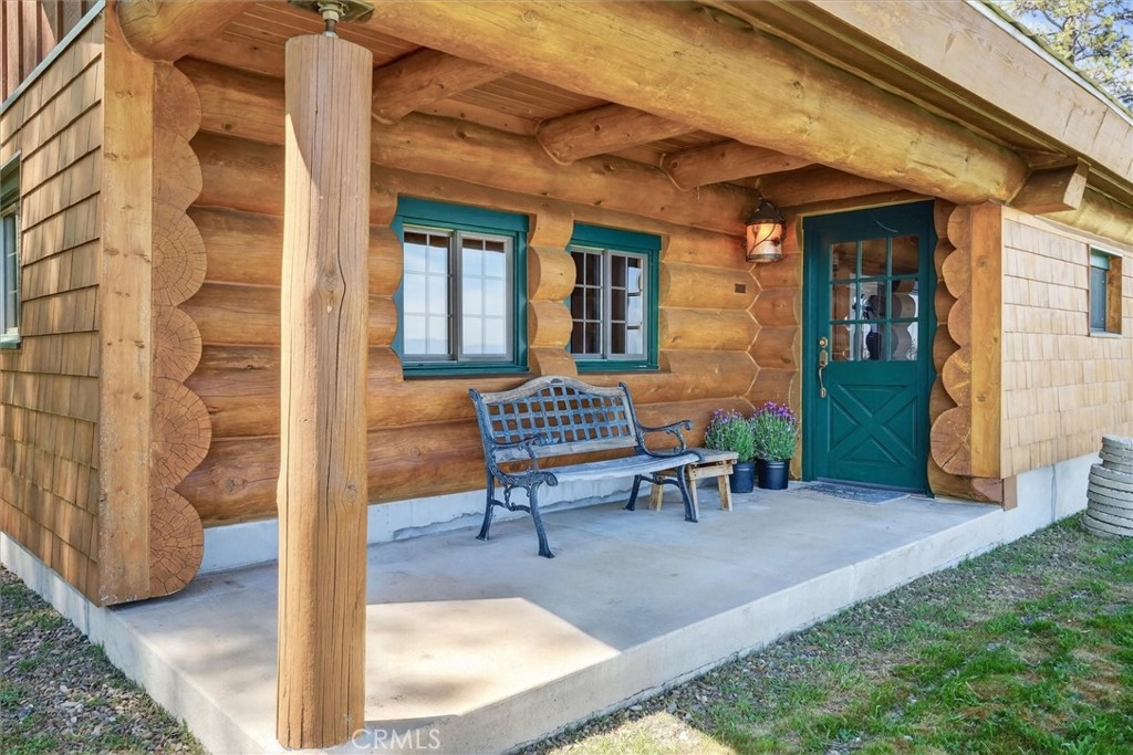 Rustic log home porch with a teal entry door, timber roof, and metal bench.