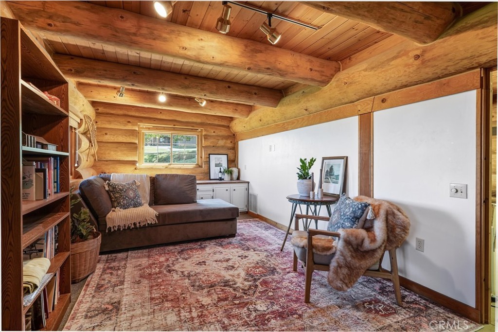 Living room with exposed log walls, a timber ceiling, built-in bookshelves, and a patterned rug.