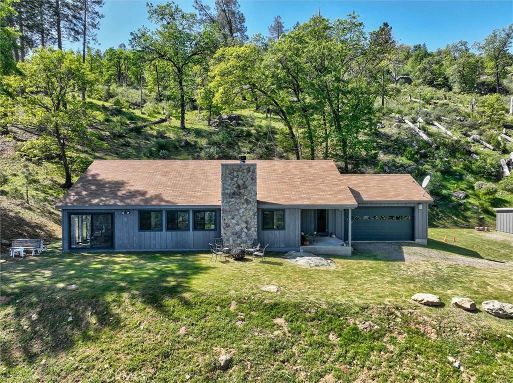 Single-story home with a stone chimney and attached garage in a wooded hillside clearing.