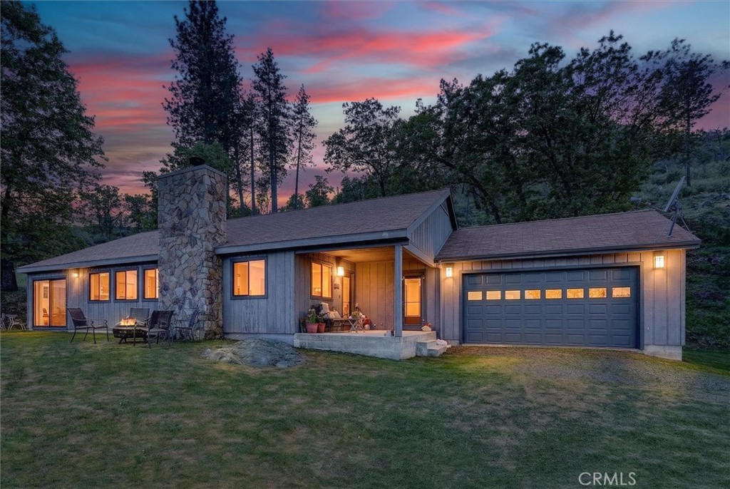 Gray home with a stone chimney and two-car garage beneath a pink sunset sky.