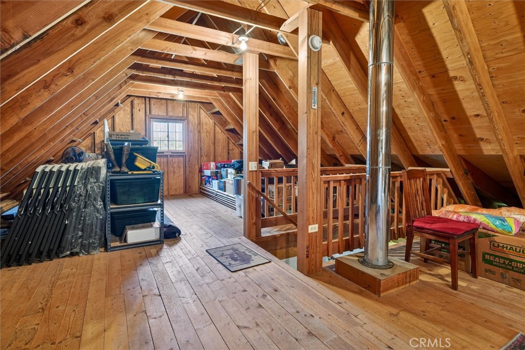 Wood-paneled attic with exposed rafters, a railing around an opening, and a metal stovepipe.