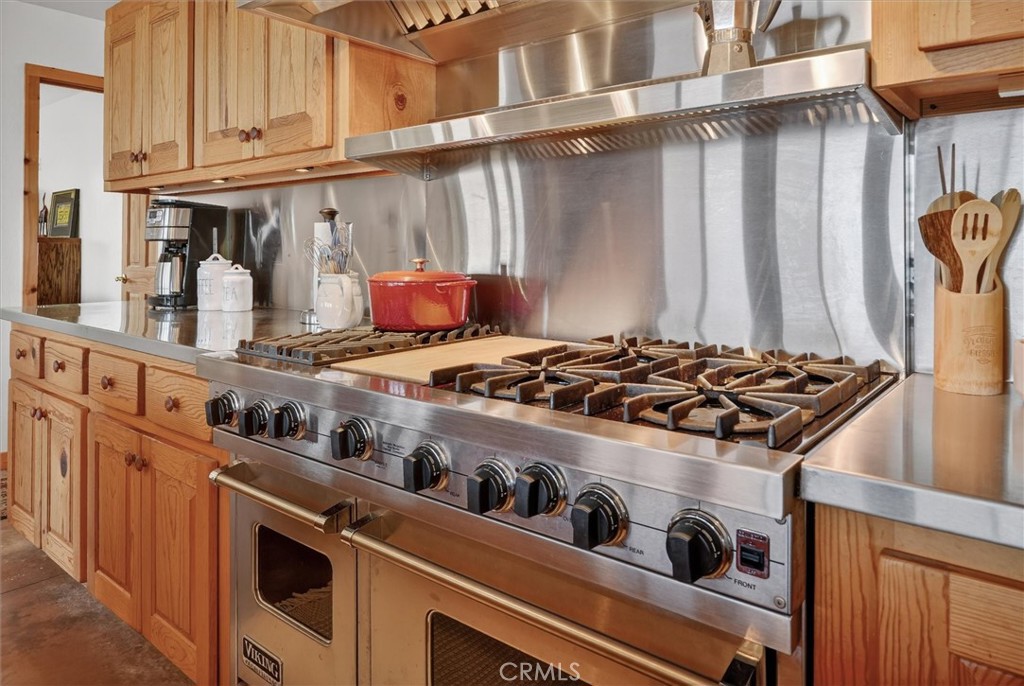 Kitchen with a large stainless-steel Viking gas range, stainless backsplash, and honey-toned wood cabinets.