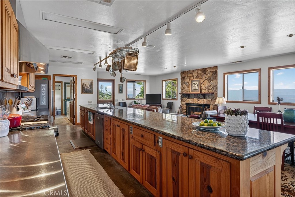 Kitchen with long granite island, wood cabinetry, stone fireplace, and mountain views through large windows.