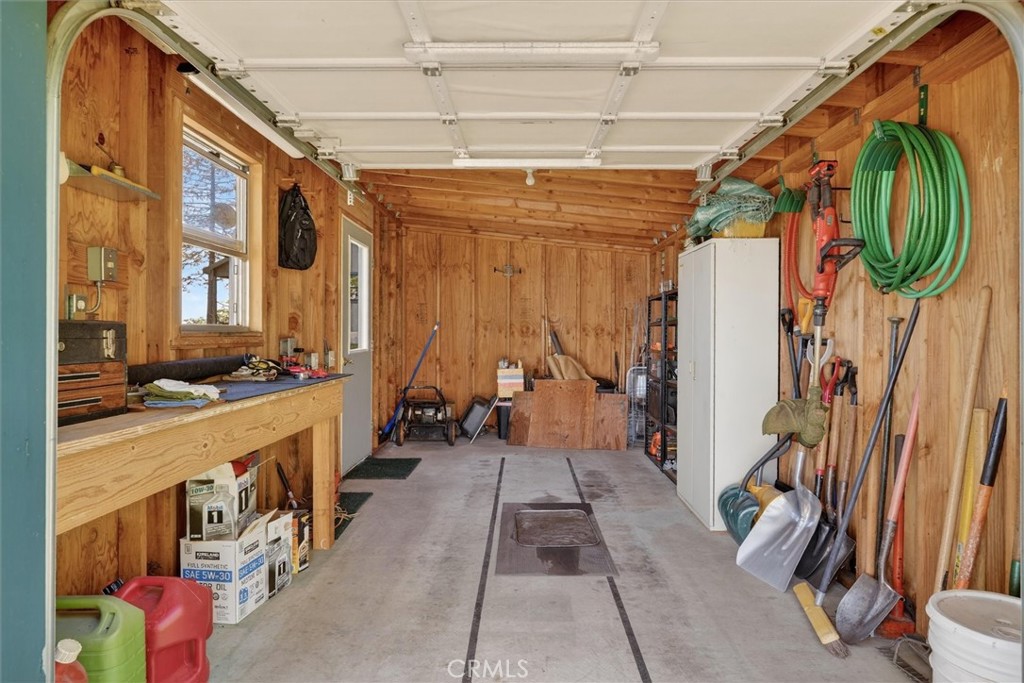 Wood-paneled garage with a workbench, storage cabinet, garden tools, and coiled green hose.