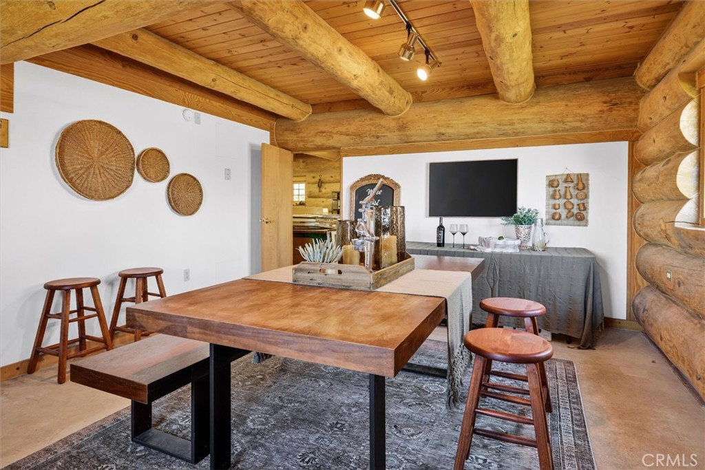 Rustic log-home room with a large wooden table, stools, and a television.