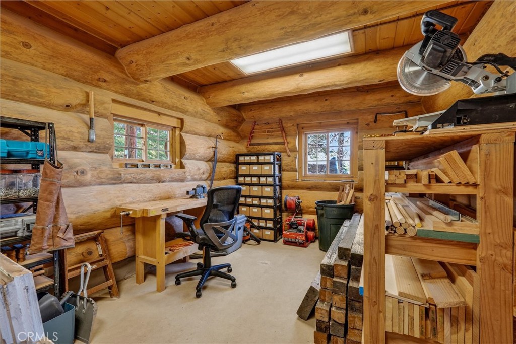 Log-cabin woodworking workshop with lumber shelves, workbenches, and a miter saw.