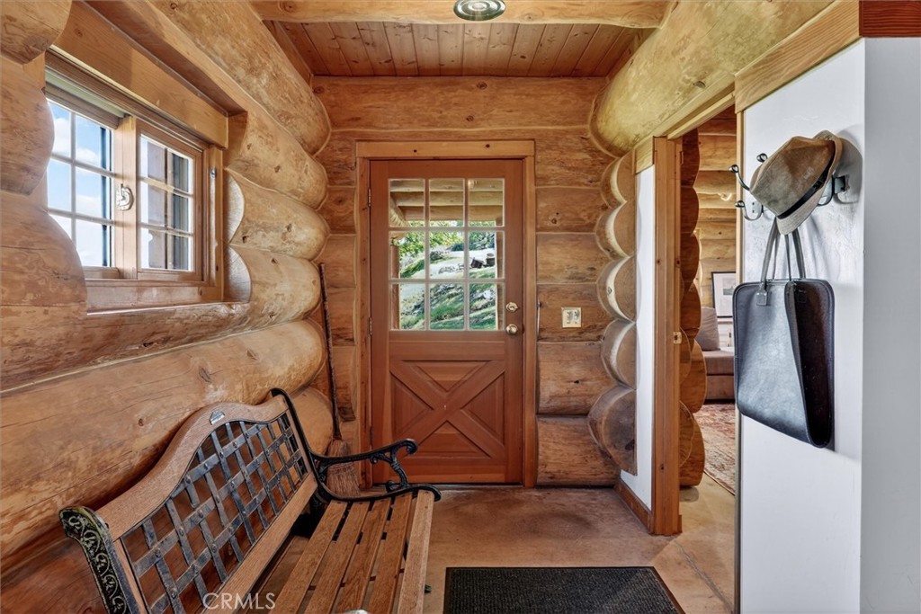 Log cabin entryway with a wooden bench, multipane front door, and hats and bags on wall hooks.