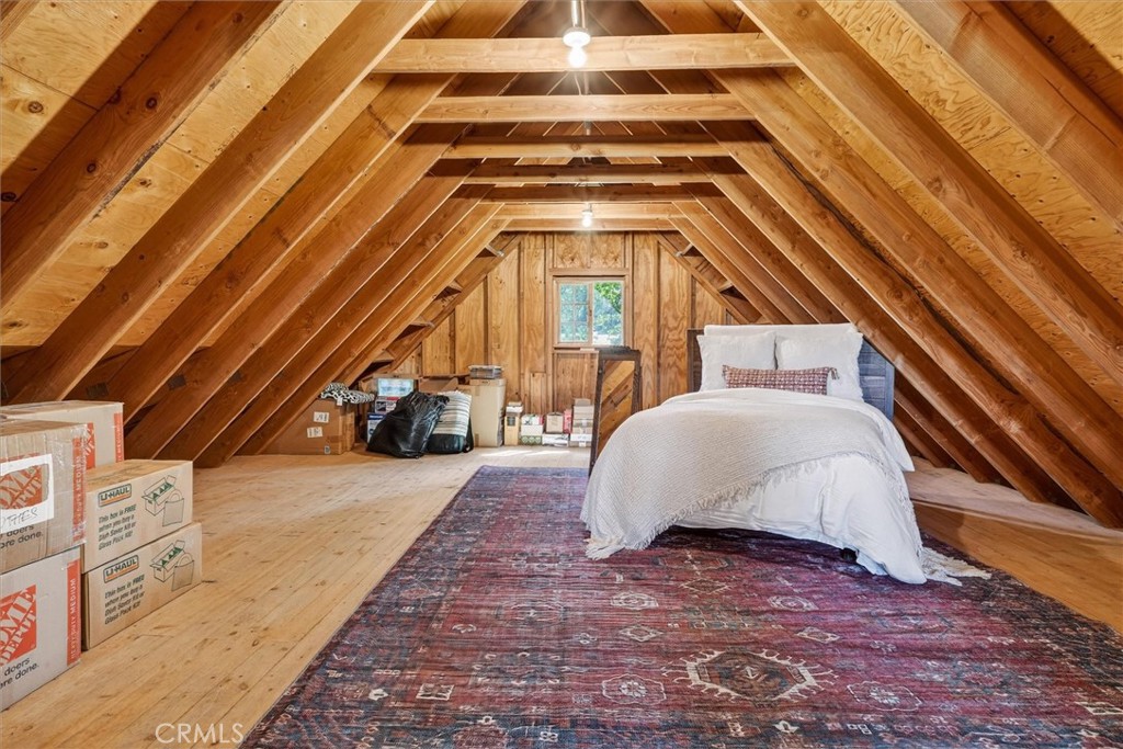 Attic bedroom with exposed timber rafters, a bed, patterned rug, and moving boxes.